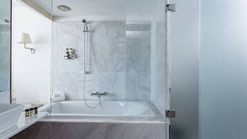 A modern bathroom with a glass-enclosed shower, a white bathtub, and a marble-tiled wall.