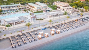 Vue aérienne d’un hôtel situé sur la côte, avec une piscine, des espaces de détente au bord de la plage et une route qui longe la plage.