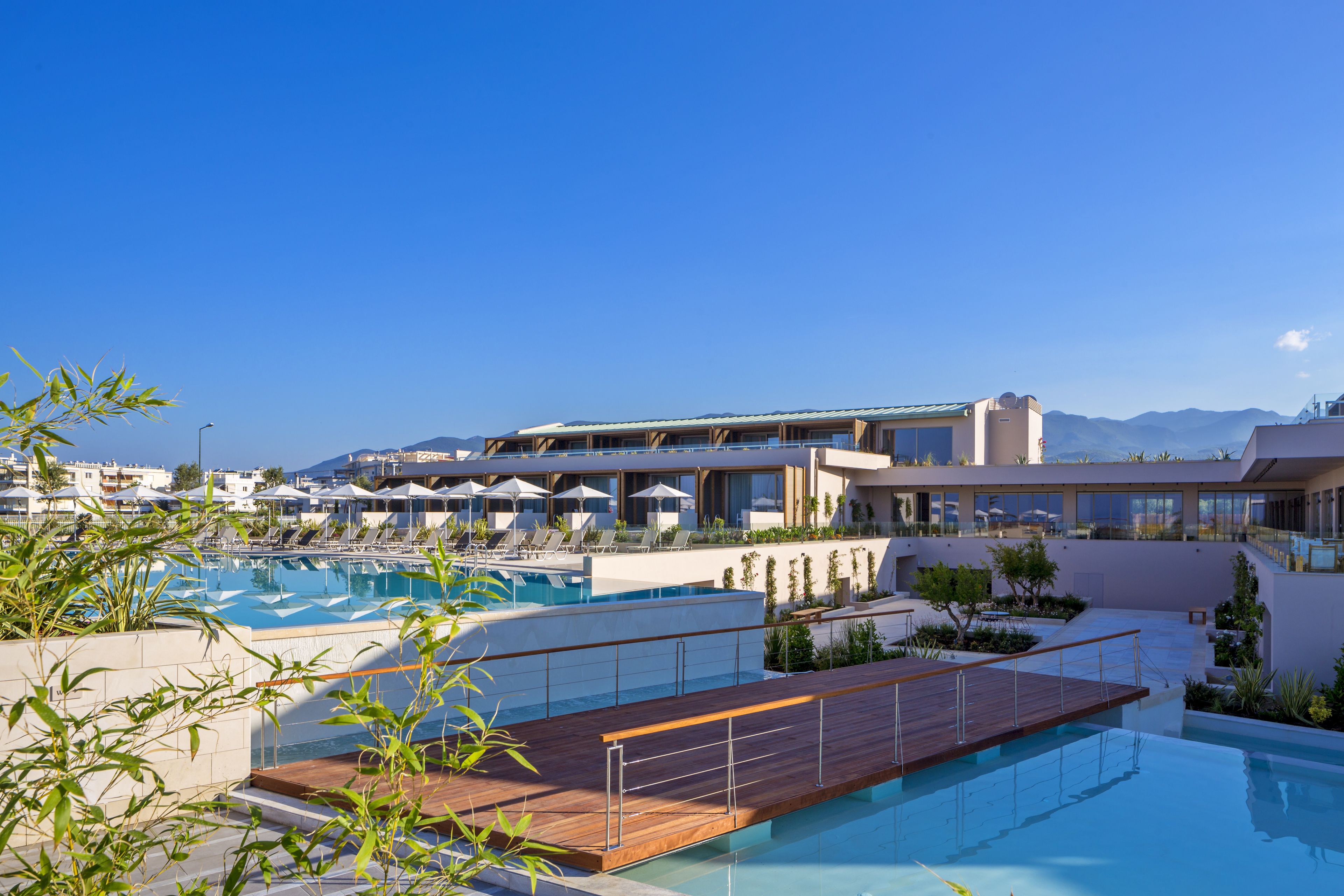 A rooftop pool area with lounge chairs and umbrellas, surrounded by buildings and mountains.