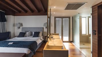 A modern hotel room with a large bed, bedside lamps, a wooden floor, a built-in sink, and a shower area.