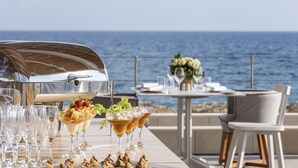Une table dressée pour un repas avec vue sur l’océan, un barbecue et un arrangement floral.