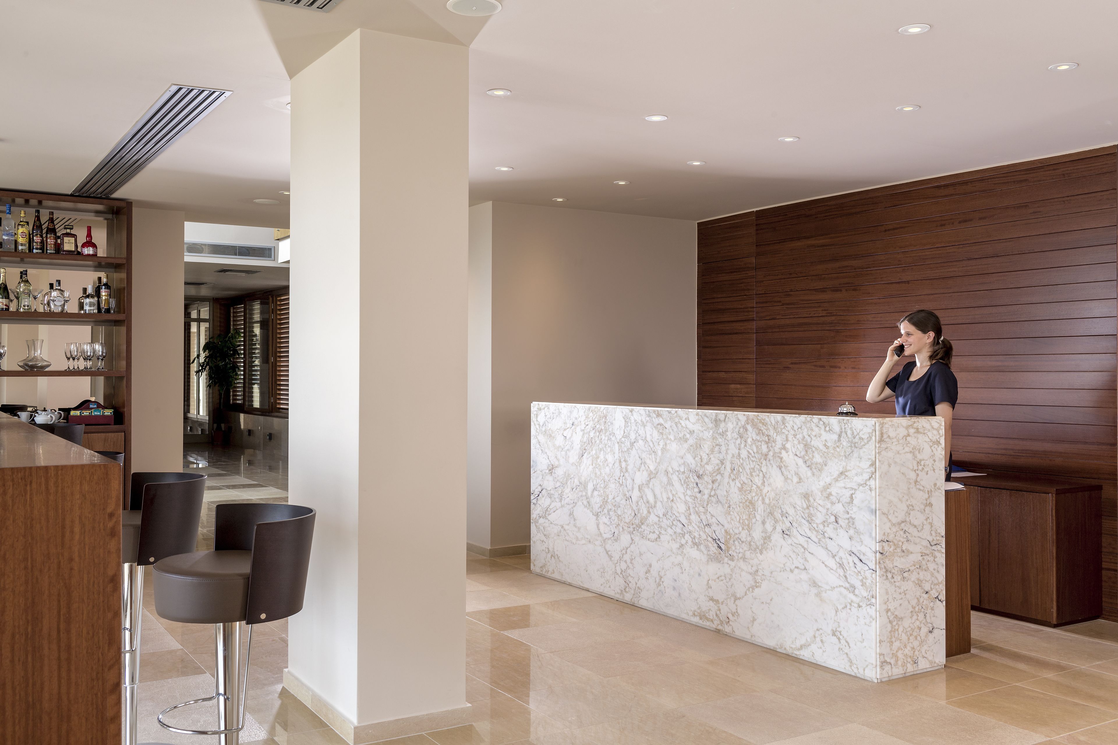 Uma área de recepção com balcão de mármore, painel de parede em madeira e um bar com banquetas.