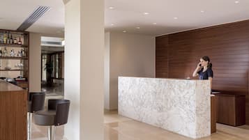 Uma área de recepção com balcão de mármore, painel de parede em madeira e um bar com banquetas.