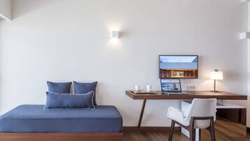 A modern bedroom with a bed, a desk with a laptop, a chair, and a TV on the wall.