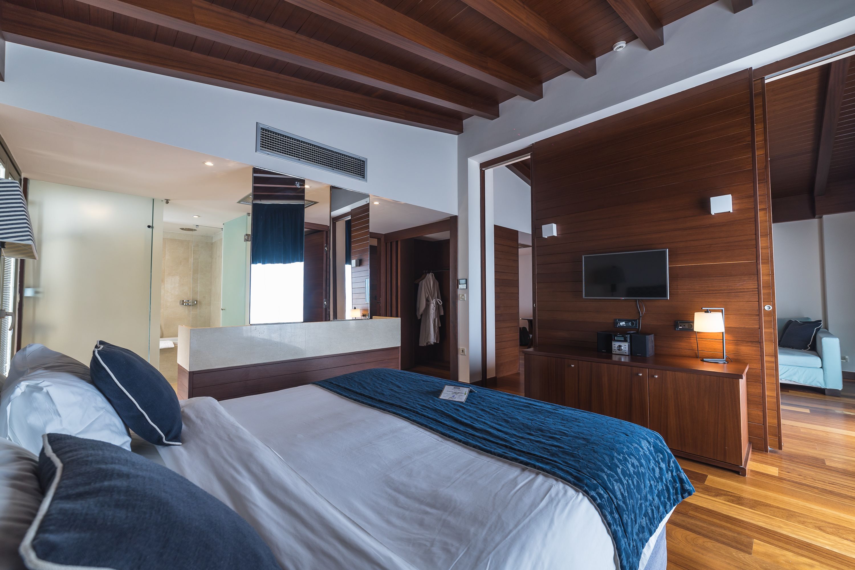 Una habitación de hotel moderna con una cama grande, vigas de techo de madera, un televisor y un escritorio con lámpara.