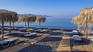 Une plage avec des passerelles en bois, des chaises longues et des parasols en chaume.