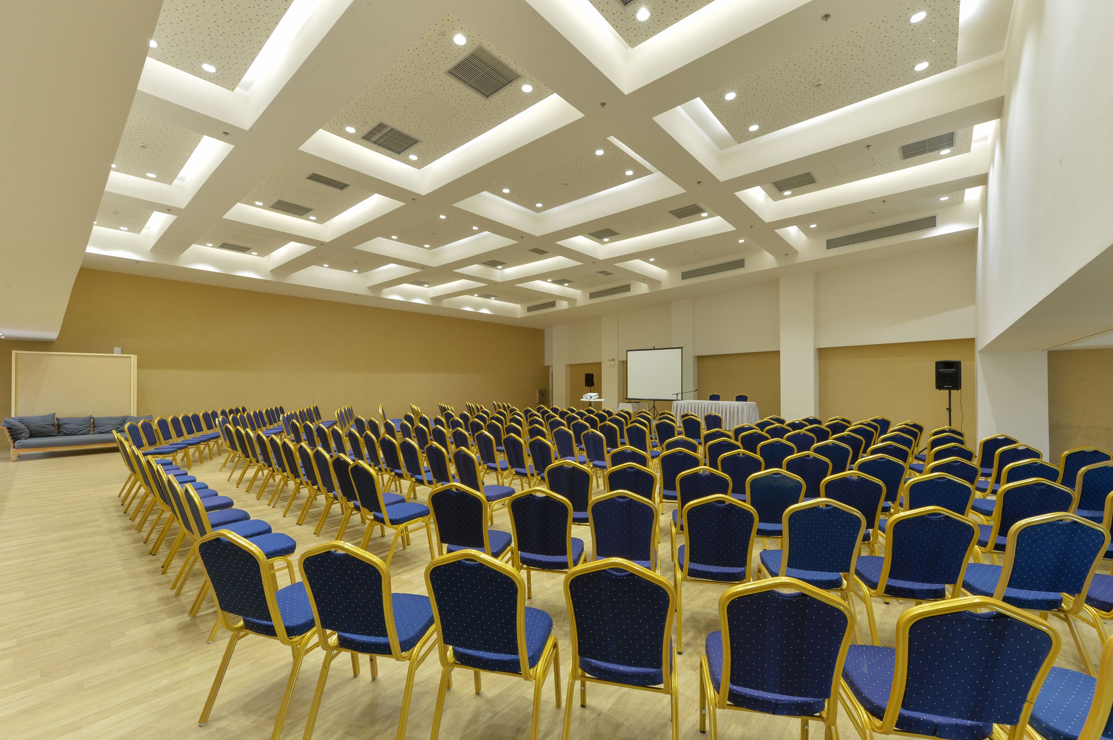 A conference room with rows of blue chairs and a stage with a projector.