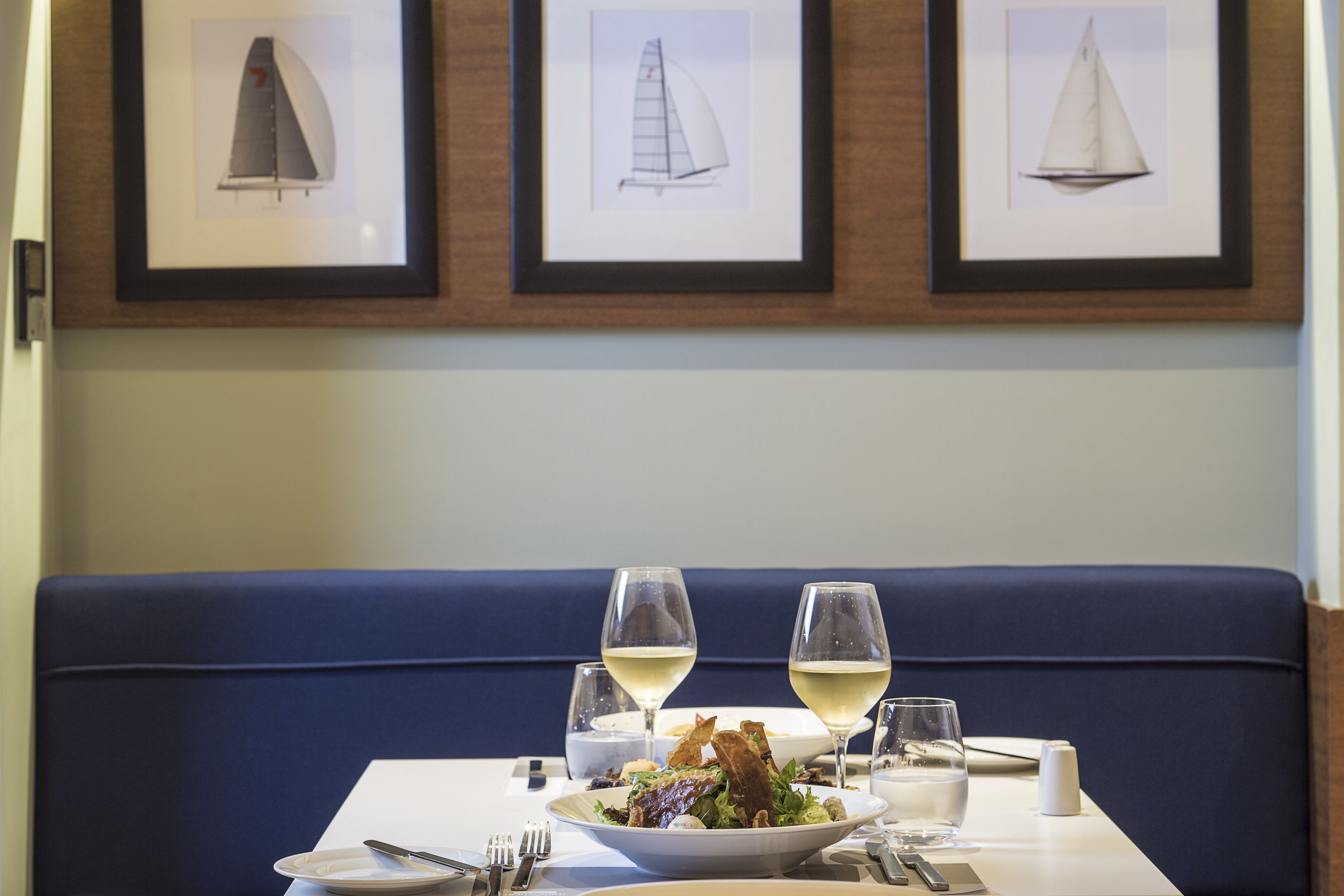 A dining table with a salad, two wine glasses, and a white plate.