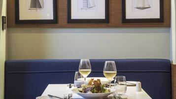 A dining table with a salad, two wine glasses, and a white plate.