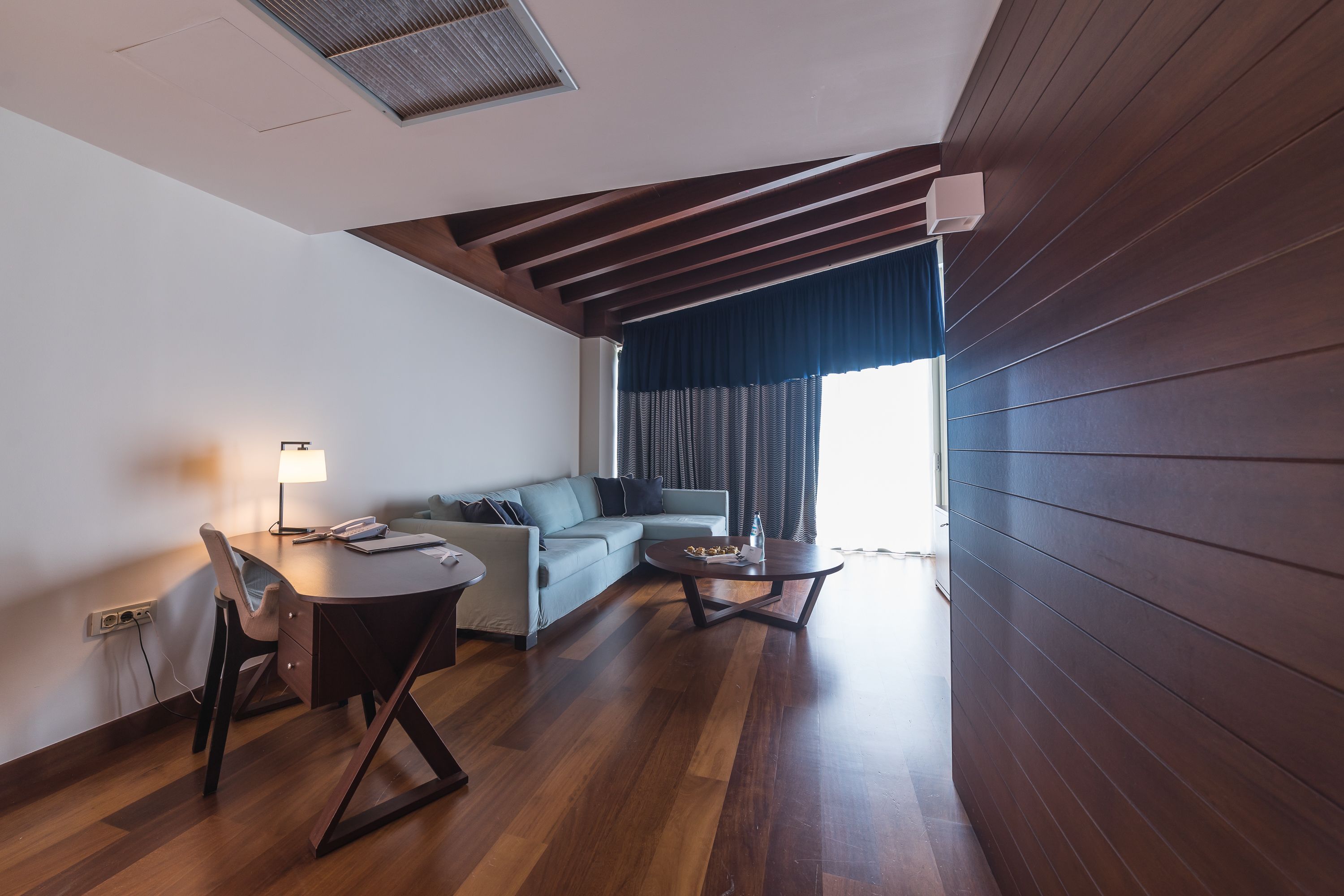 A modern living room with a wooden floor, a round coffee table, a sofa, and a dining table with chairs.