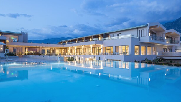 Un hôtel moderne doté d’une grande piscine, de nombreux balcons et offrant une vue sur les montagnes.