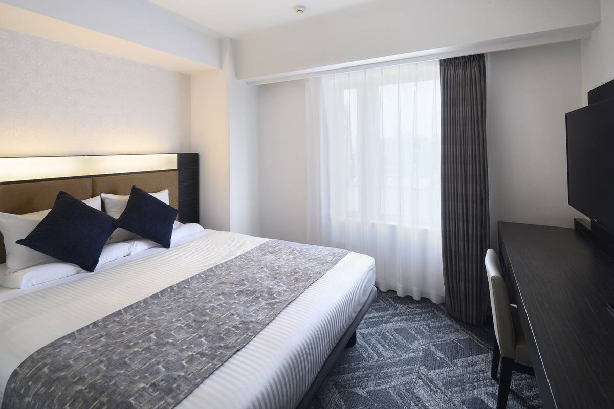 A hotel room with a large bed, a desk, a television, and a window with curtains.