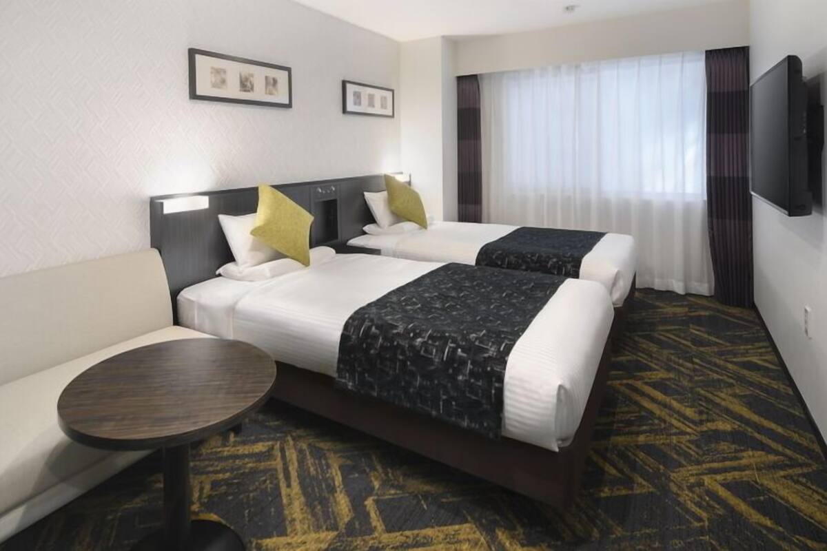 A hotel room with two beds, a sofa, a small table, and a TV.