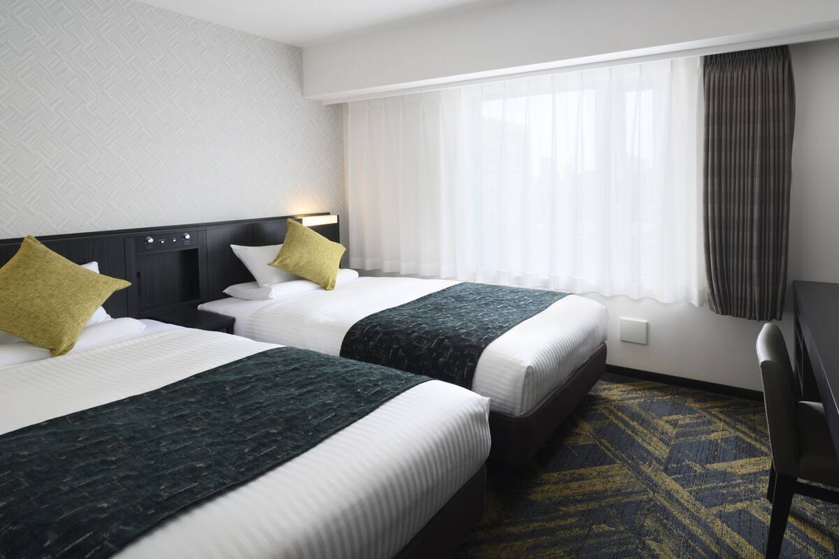 A hotel room with two beds, a desk, and a TV.