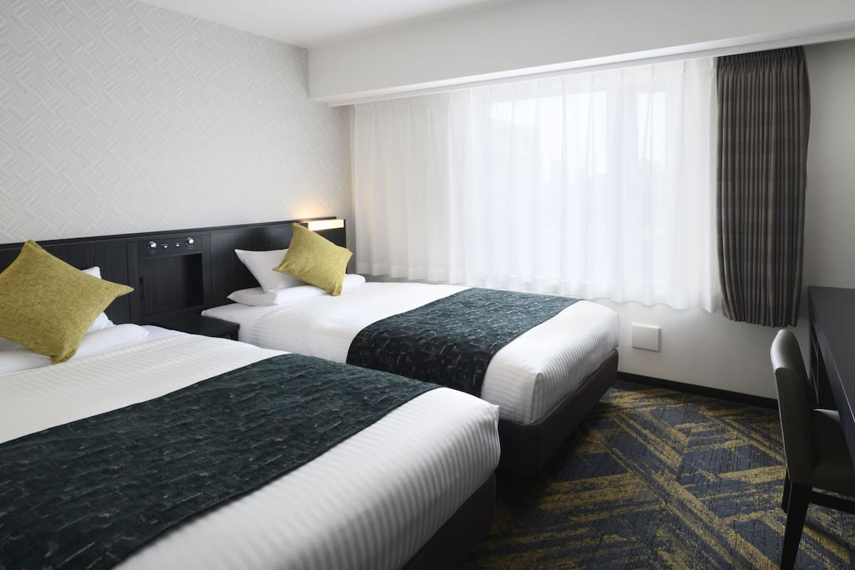 A hotel room with two beds, a desk, and a TV.