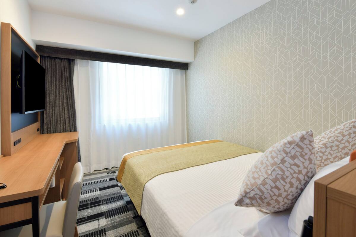 Une chambre d’hôtel avec un lit, un bureau, une télévision et une fenêtre avec des rideaux.