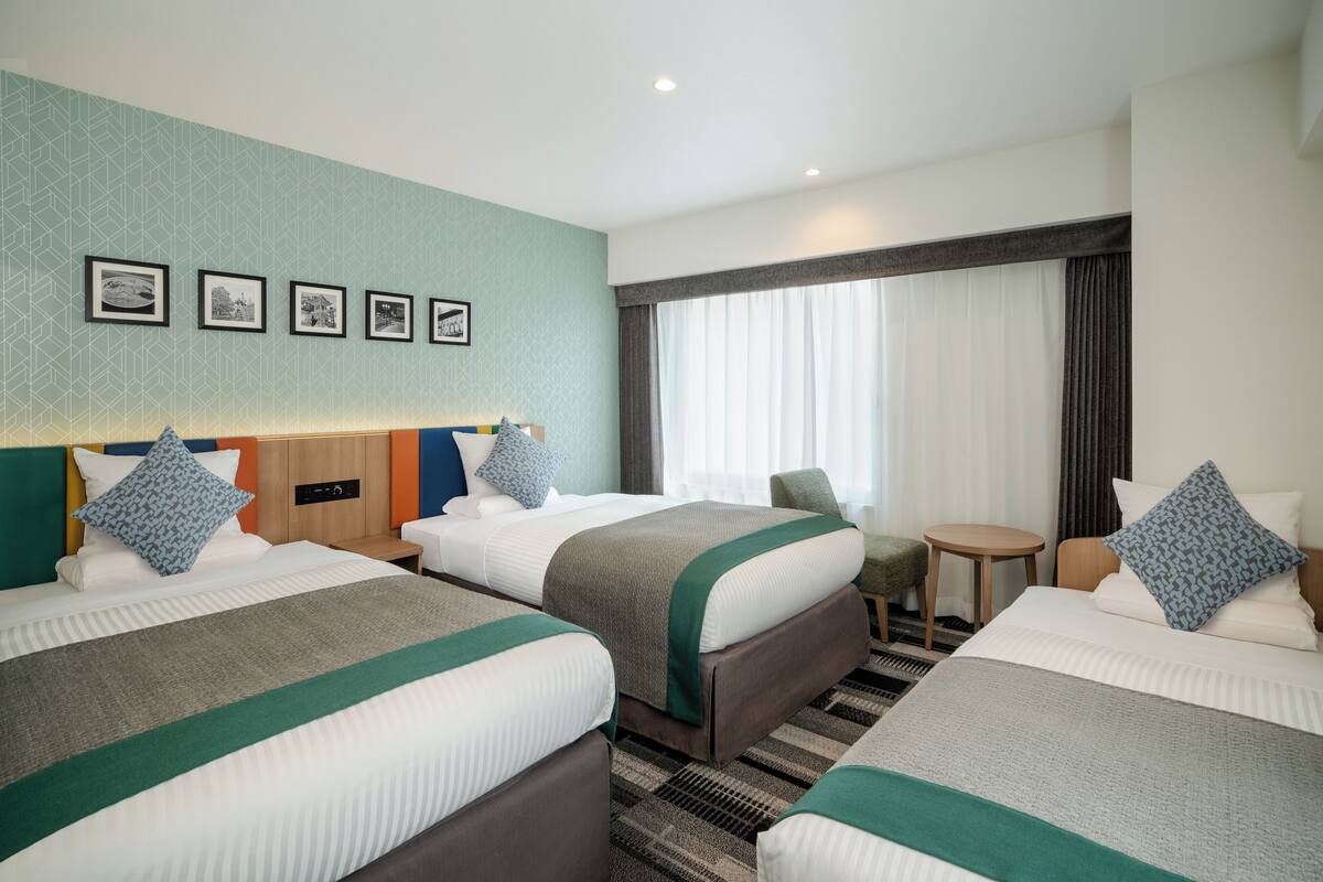 Une chambre d’hôtel avec deux lits, une petite table et une fenêtre avec des rideaux.