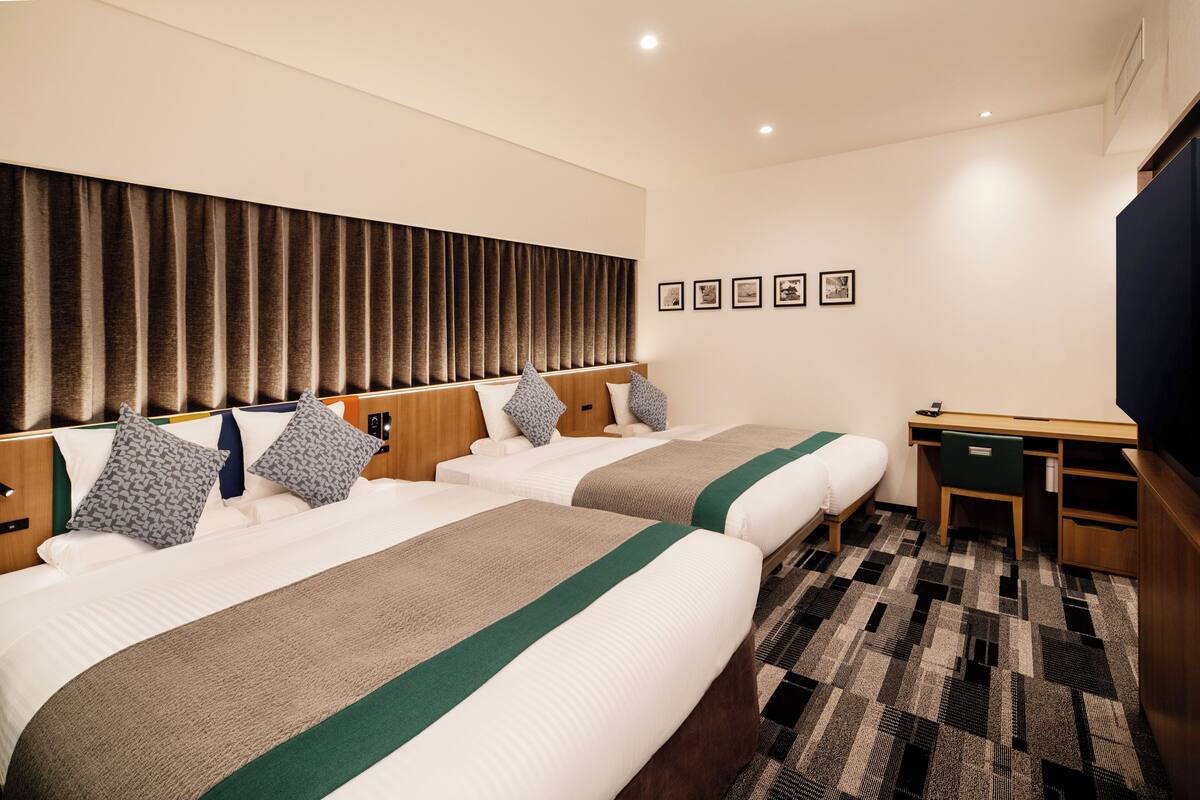 Une chambre d’hôtel avec deux lits, un bureau et une grande fenêtre avec des rideaux.