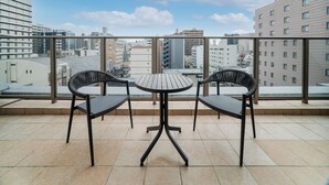 Uma varanda com duas cadeiras e uma mesa, com vista para um horizonte urbano repleto de edifícios.