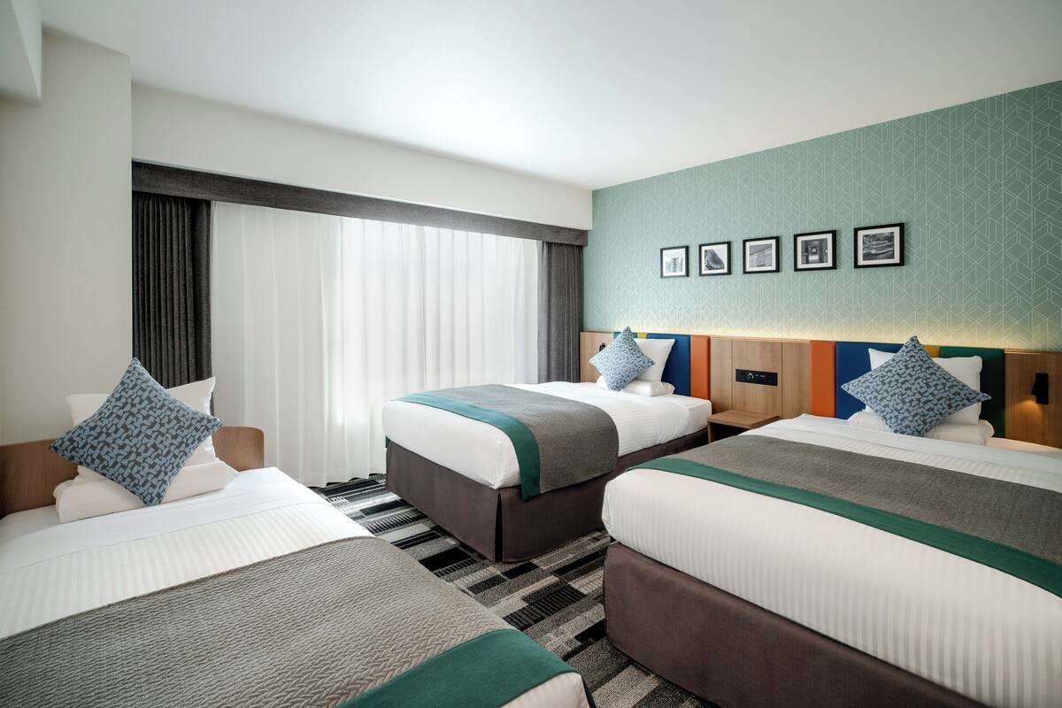 Une chambre d’hôtel avec deux lits, une grande fenêtre avec des rideaux et un mur décoré de tableaux encadrés.
