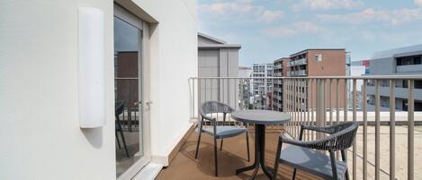 A balcony with two chairs and a table, a sliding glass door, and a view of surrounding buildings.