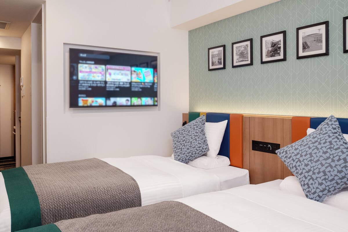 Une chambre d’hôtel avec deux lits, un téléviseur fixé au mur et des tableaux encadrés.