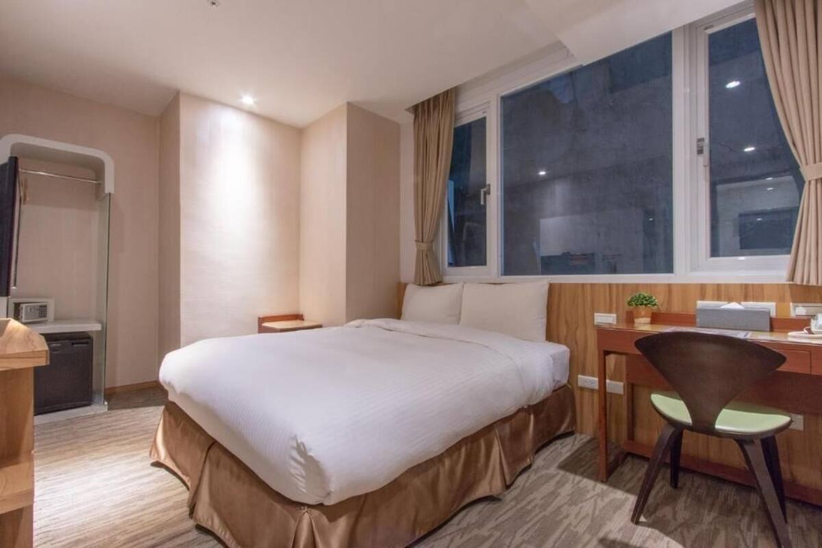 A hotel room with a bed, desk, chair, and a window with curtains.