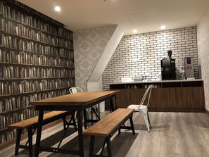 A cozy reading nook with a bookshelf, a wooden table, and a coffee machine. - Muzik Hotel - Ximending Xining Branch (Taipei)