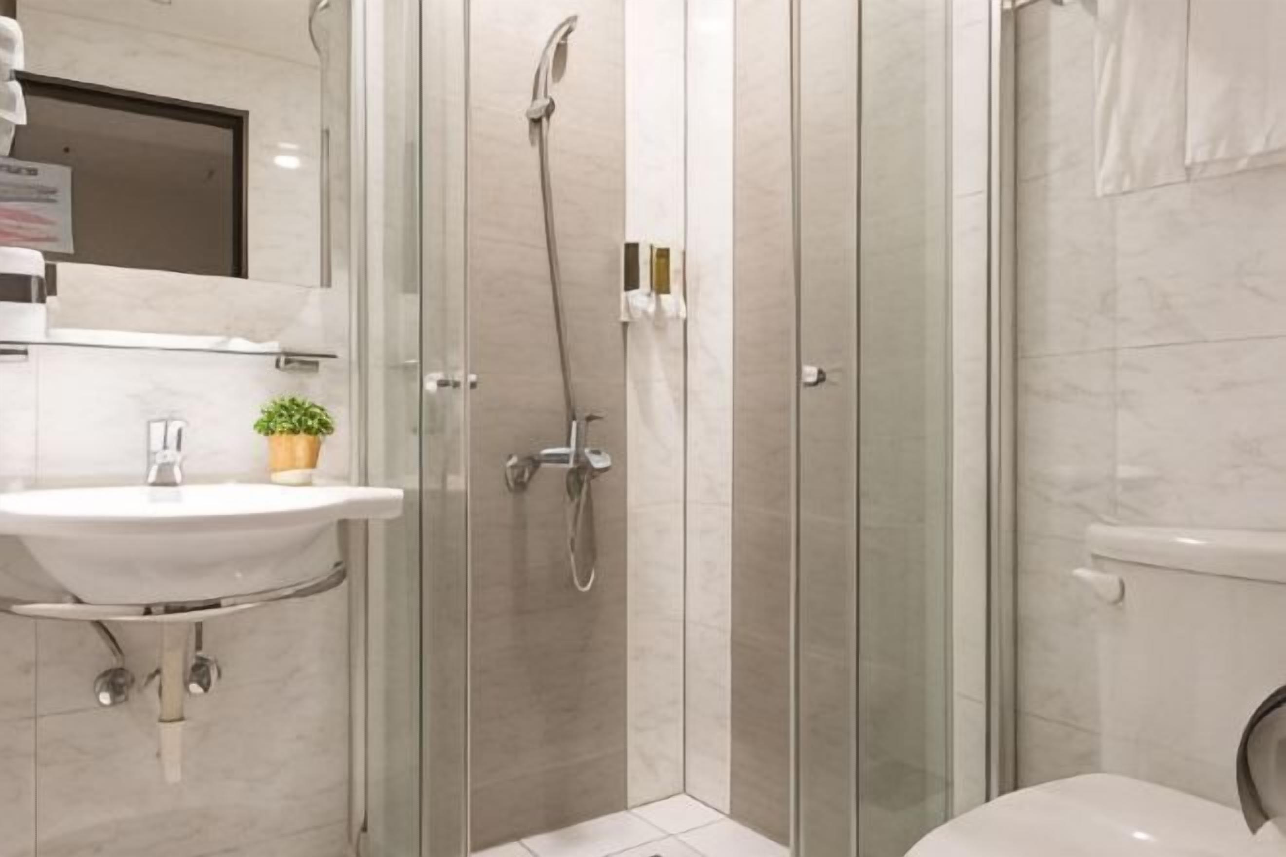 Ein modernes Badezimmer mit einer gläsernen Duschkabine, einem Waschbecken mit Spiegel und einer Toilette.