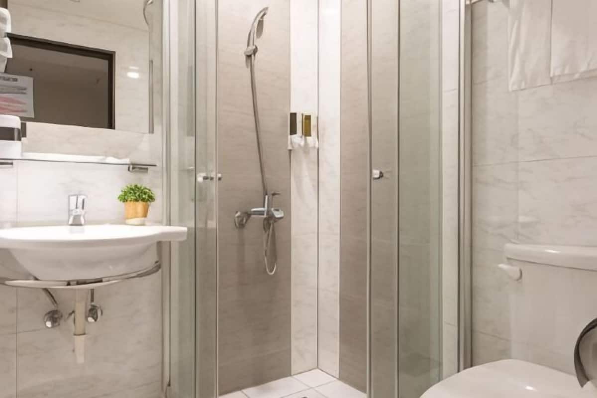 Ein modernes Badezimmer mit einer gläsernen Duschkabine, einem Waschbecken mit Spiegel und einer Toilette.