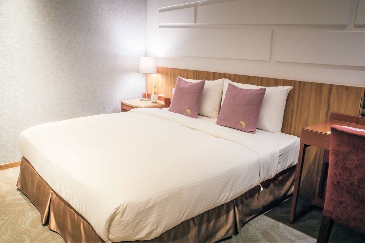 A neatly made bed with a wooden headboard, a bedside table with a lamp, and a chair.