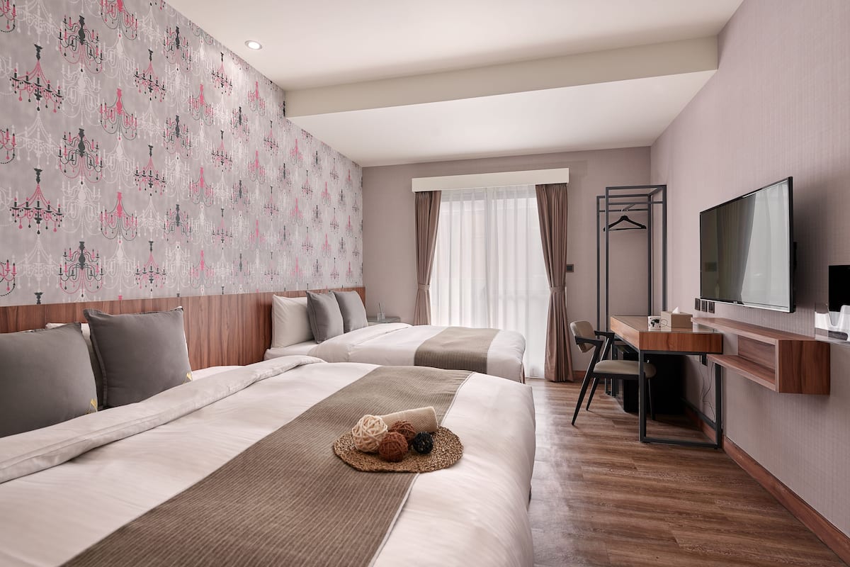 A hotel room with two beds, a desk, a TV, and a wardrobe.