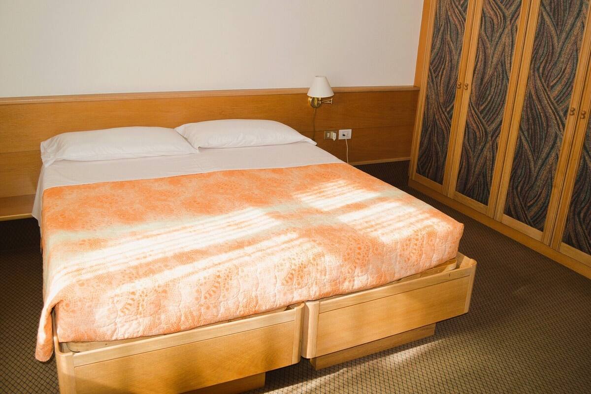 Een eenpersoonsbed met een bedsprei met patroon, een bedlampje en een garderobe met een deur met patroon.