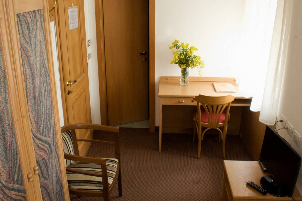 Een kleine, compacte kamer met een houten bureau, een stoel, een bed en een televisie.