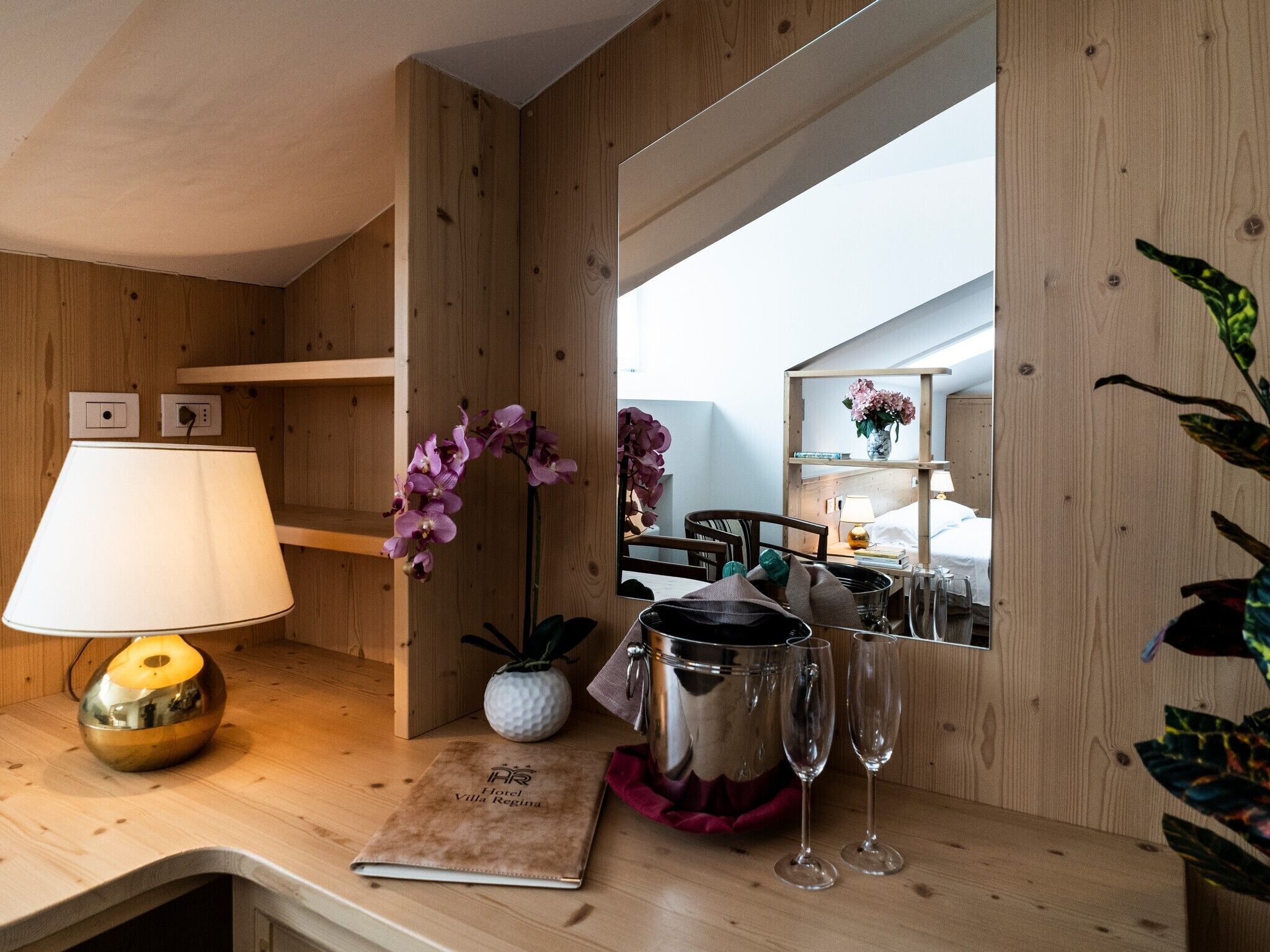 Camera d'albergo con pareti in legno, un comodino con una lampada, uno specchio, un minibar e vista sull'interno della stanza.