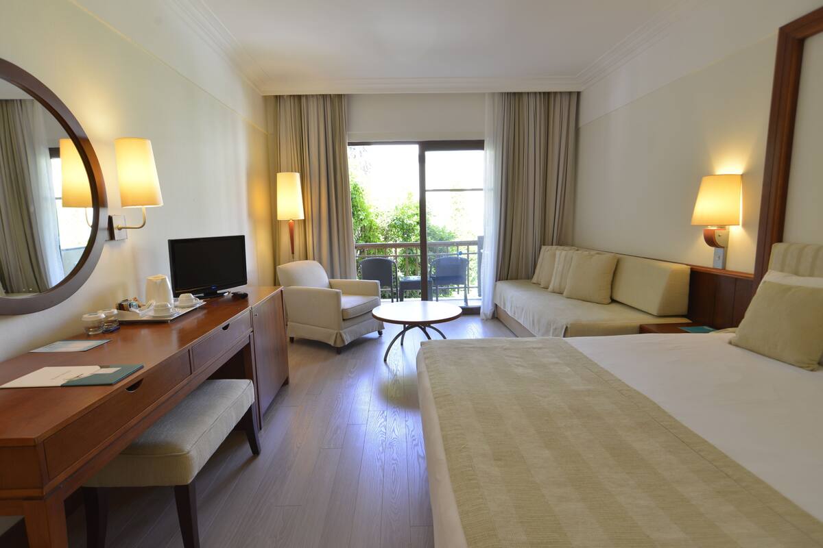 Habitación de hotel con cama, escritorio, silla, una mesita y balcón con vistas a zonas verdes.