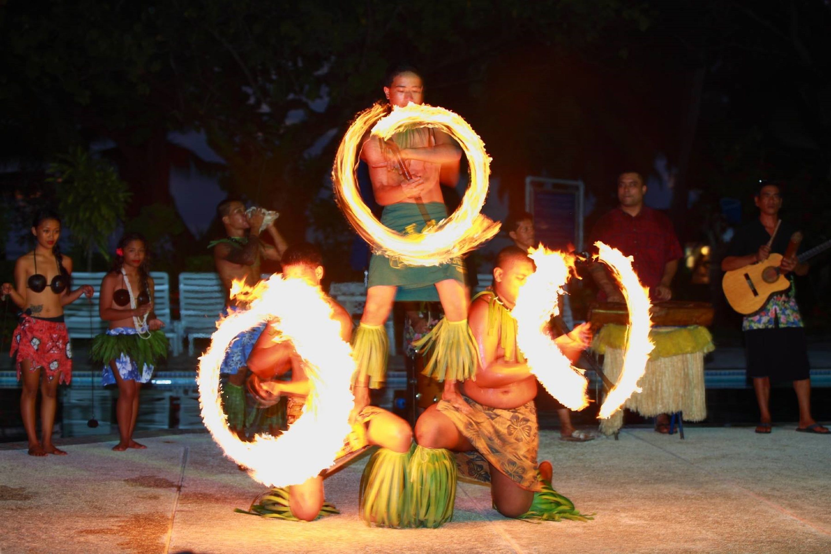 A group performing fire dance with flaming hoops, surrounded by onlookers and musicians.