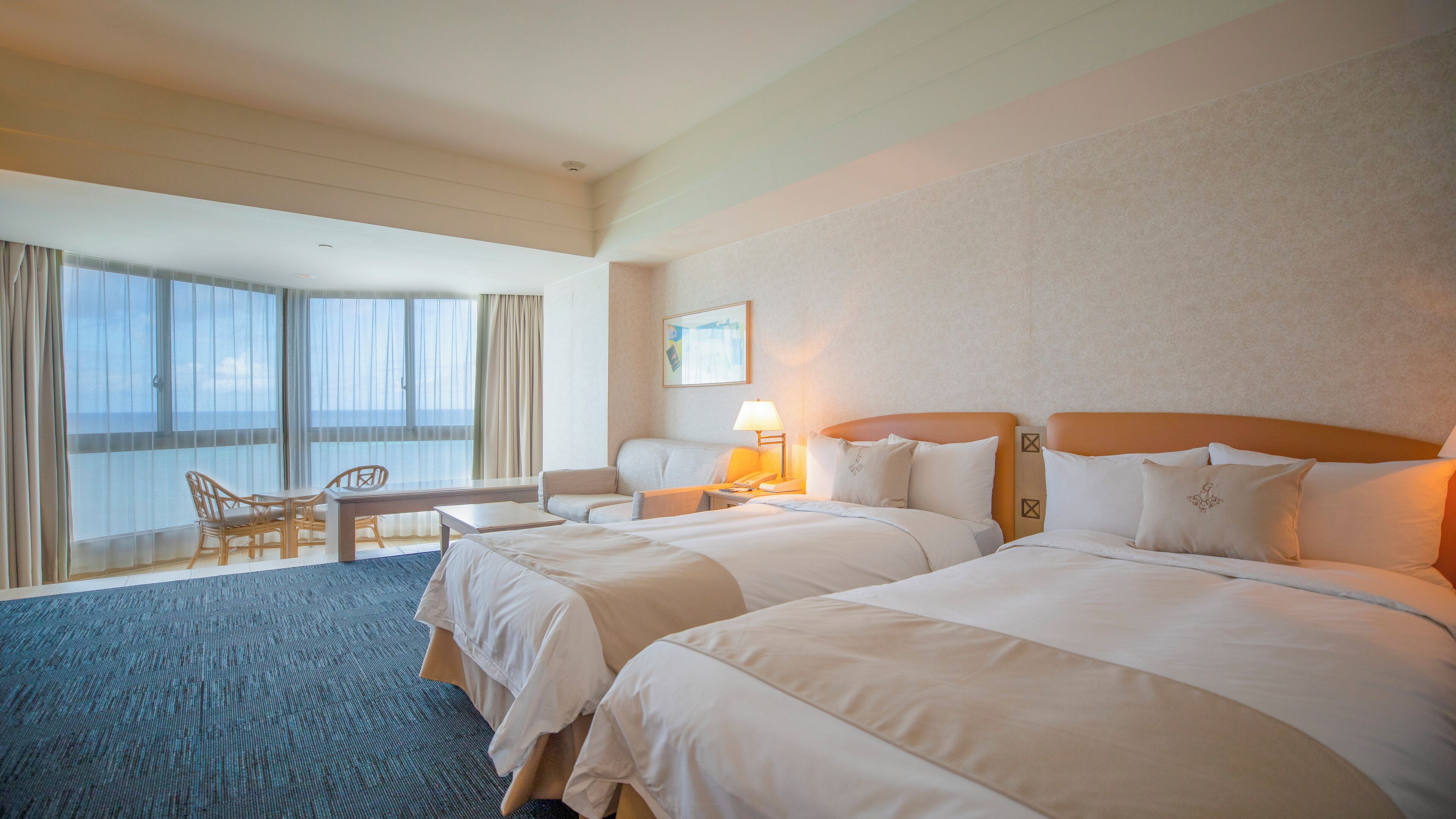 A hotel room with two beds, a desk, a chair, and a large window with curtains.