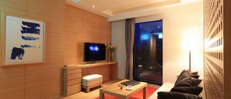 Una sala de estar moderna con un televisor de pantalla plana, muebles de madera, una alfombra roja y un ventanal grande.