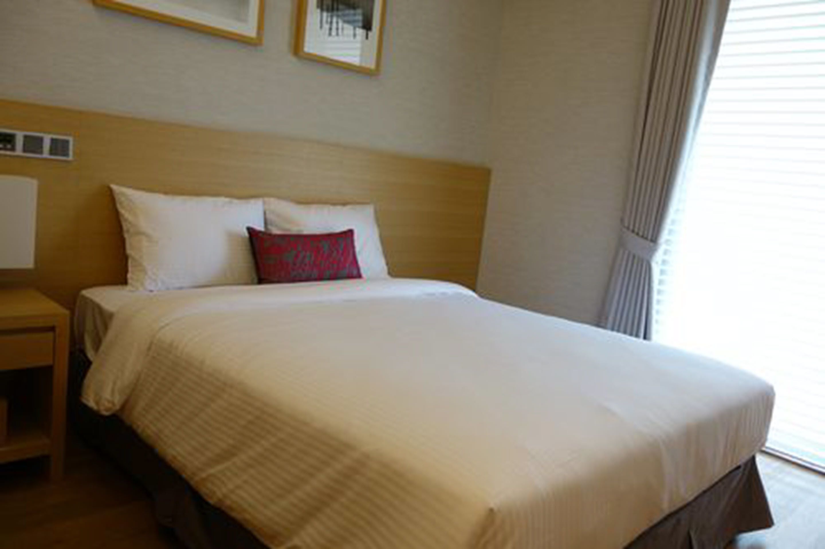 A neatly made bed with white and red pillows, a wooden headboard, and a small bedside table with a lamp.