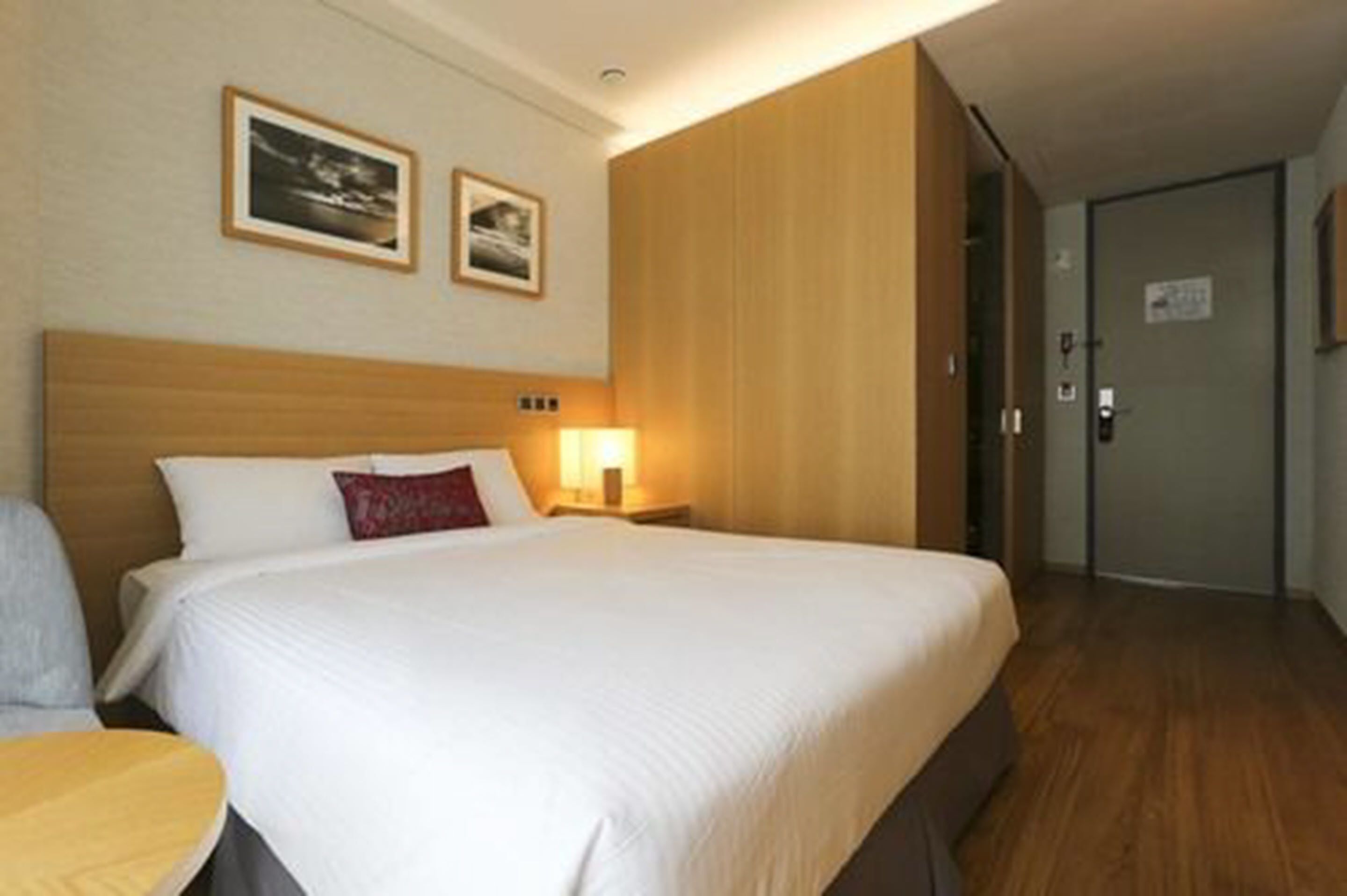 Una habitación de hotel con una cama grande, una mesita de noche y una silla. Hay dos cuadros enmarcados en la pared sobre la cama.