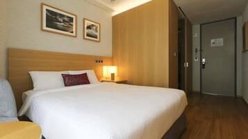 Una habitación de hotel con una cama grande, una mesita de noche y una silla. Hay dos cuadros enmarcados en la pared sobre la cama.