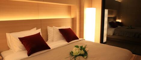Un lit bien fait, avec des oreillers blancs et rouges, une couvre-lit beige et un petit bouquet de fleurs blanches.