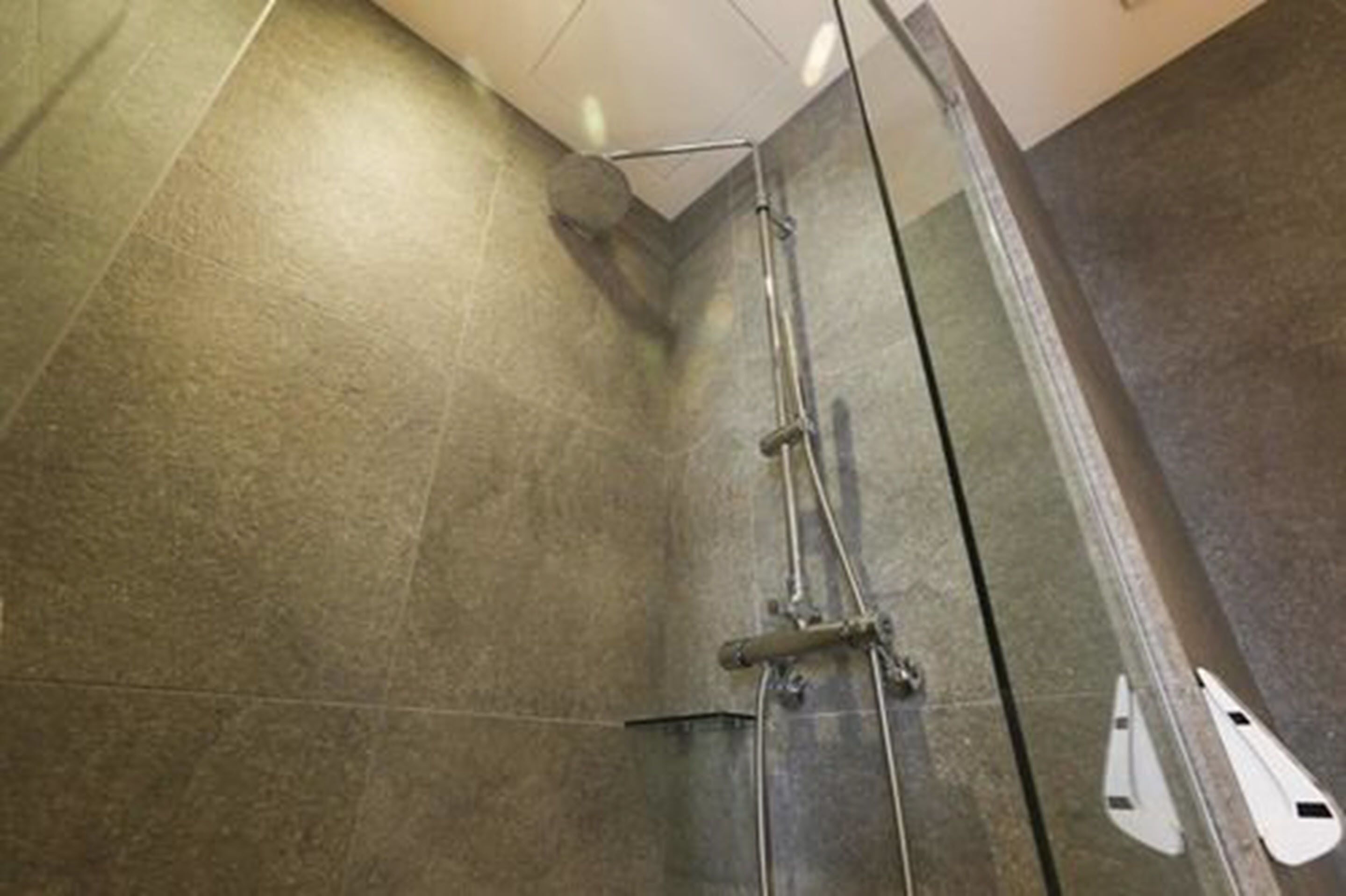 Une douche avec une porte en verre, un pommeau de douche à main et un robinet mural.