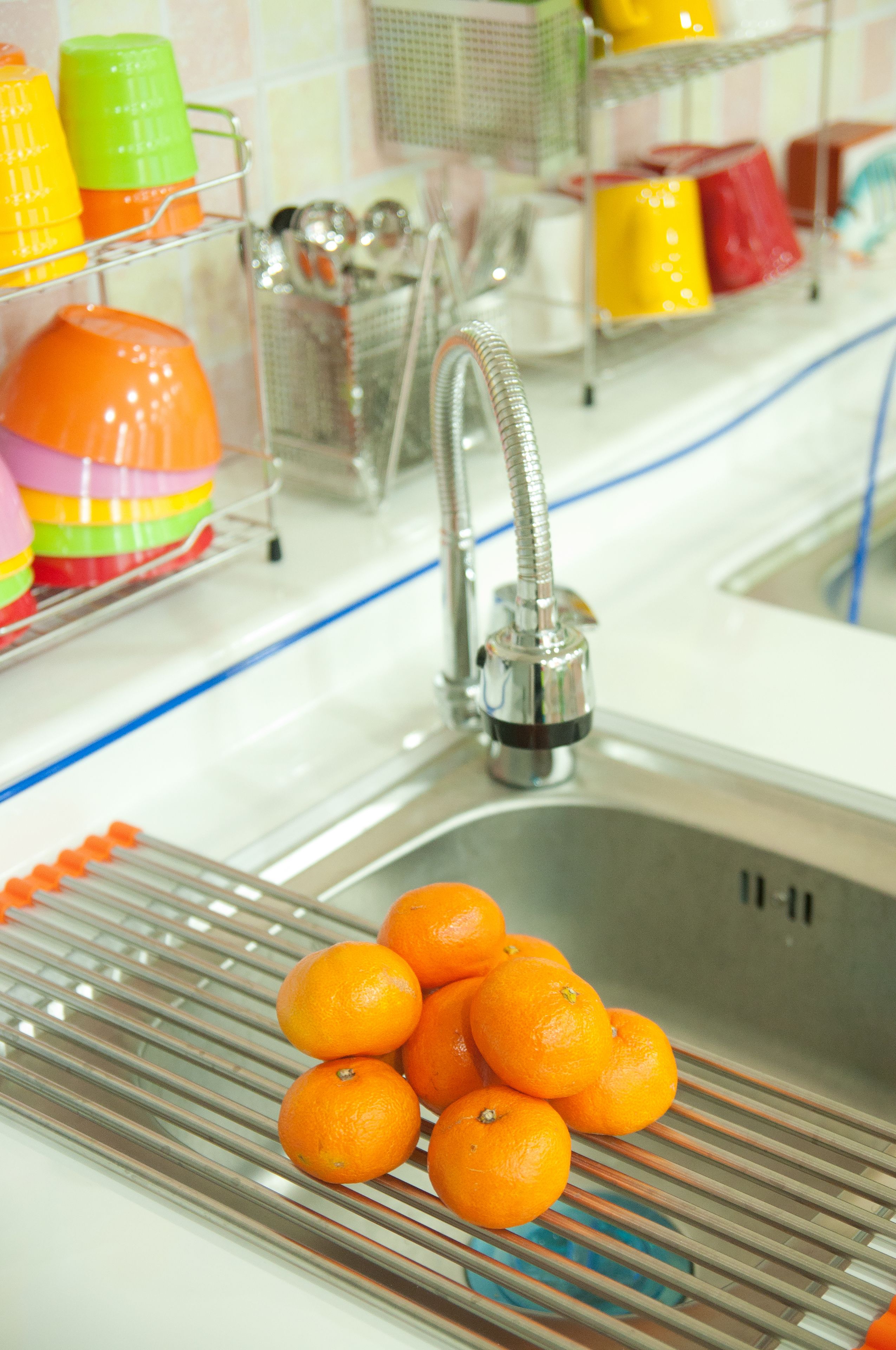 Un lavamanos de cocina con un estante metálico que sostiene naranjas y un grifo.