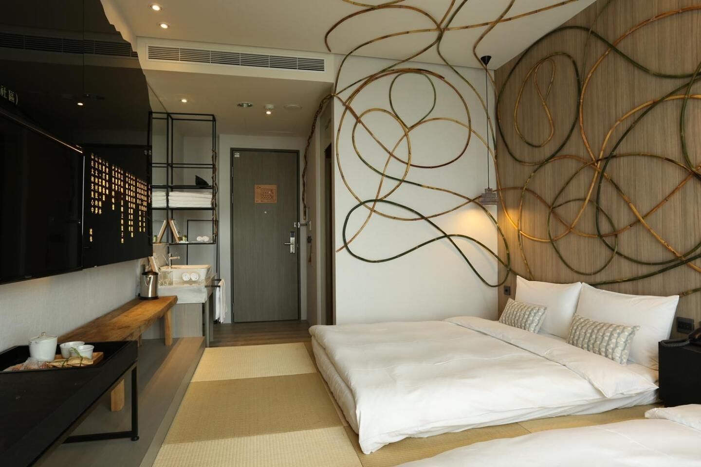 Una habitación de hotel moderna con una cama grande, un banco de madera, una pequeña cocina y una pared con arte abstracto.