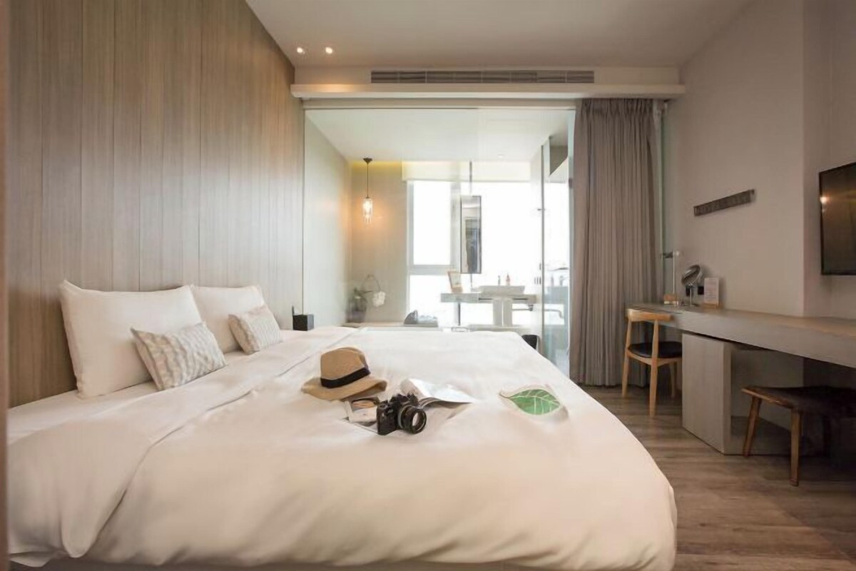 A modern hotel room with a large bed, a desk, and a view of the outside.