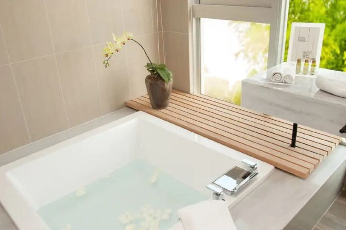 A modern bathroom with a large bathtub, wooden slats, a potted orchid, and toiletries on a marble counter.
