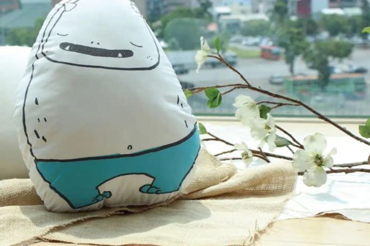 A pillow with a cartoon character design placed on a window sill with a view of a cityscape.