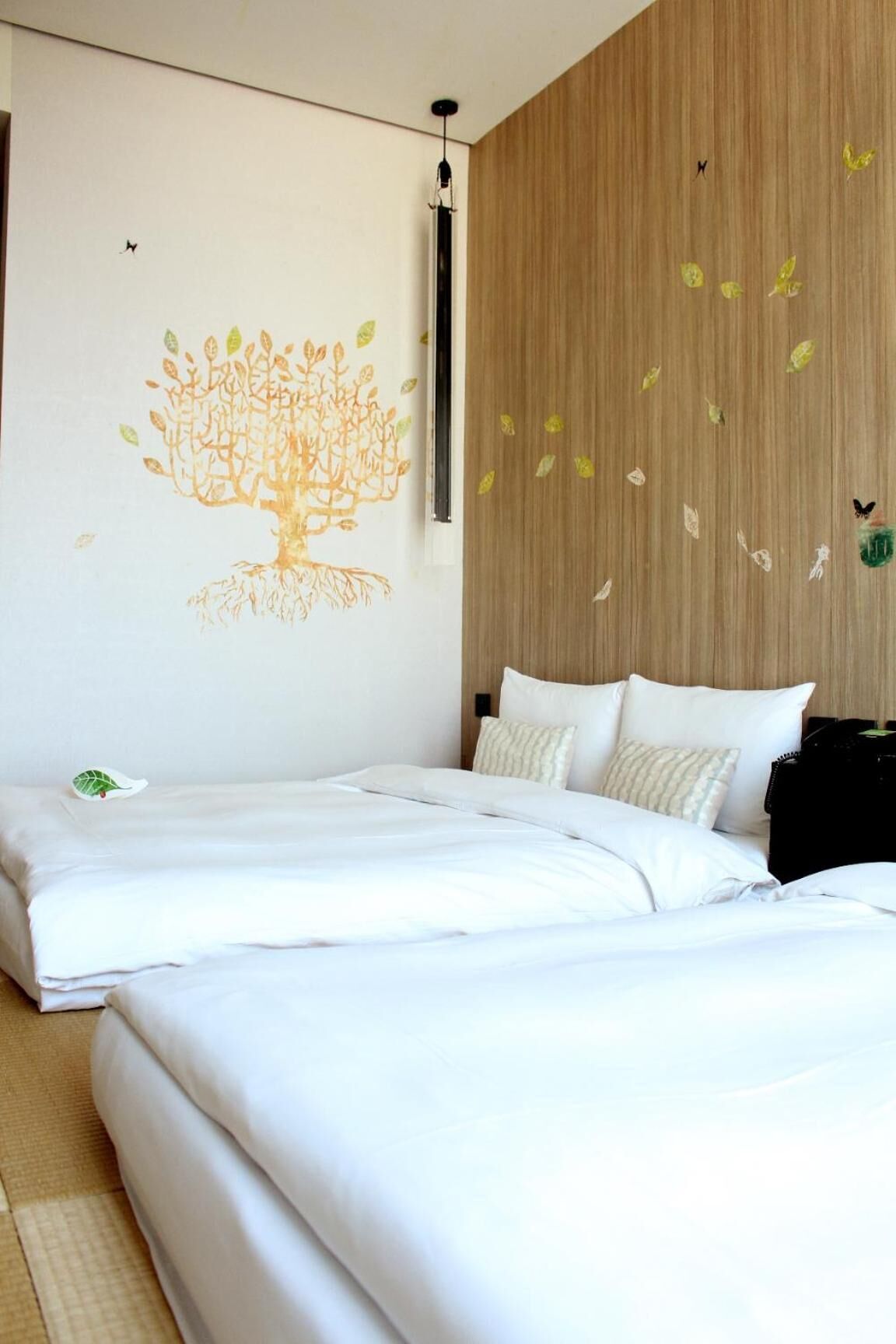 A modern hotel room with a large bed, a wooden accent wall, and a wall mural of a tree with leaves.